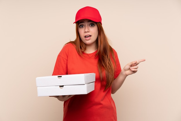 Livraison de pizza adolescent fille tenant une pizza sur un mur isolé pointant vers les latéraux ayant des doutes