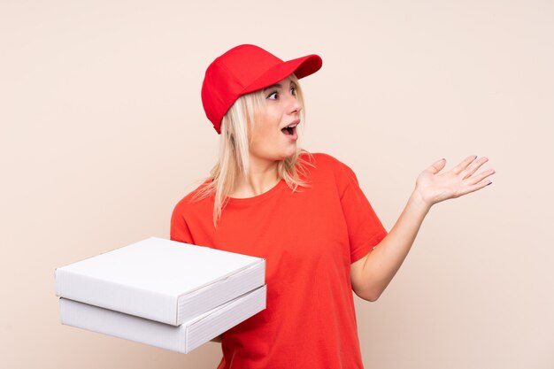 Livraison de pizza femme russe tenant une pizza sur un mur isolé avec une expression faciale surprise