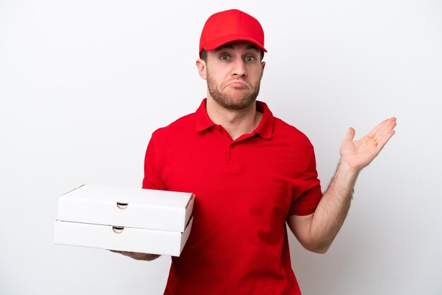 Livraison de pizza homme caucasien avec uniforme de travail ramasser des boîtes de pizza isolé sur fond blanc ayant des doutes tout en levant les mains