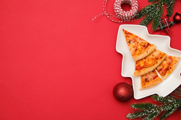 Photo livraison de pizza pour le concept de noël. arbre de noël comestible à base de pizza margarita sur fond rouge avec des décorations