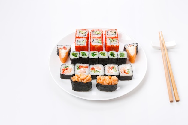 Livraison de plats traditionnels japonais. Ensemble de sushis servis sur assiette blanche et baguettes de côté. Rouleaux colorés et assortiment de gunkan sur fond blanc, pov, espace pour copie