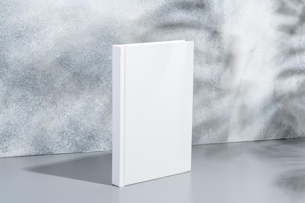 Livre blanc à couverture rigide sur fond gris avec des ombres