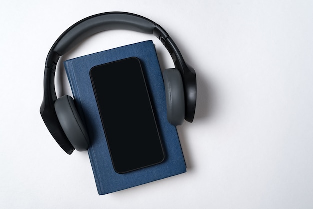 Livre bleu, écouteurs et téléphone. Concept de livres électroniques et audio. Espace de copie de fond blanc.