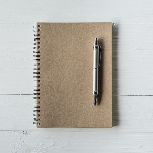 livre brun et un stylo sur une table en bois blanc