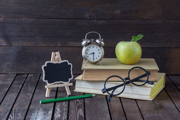 livre, un crayon vert, un réveil, une pomme verte, des lunettes et un tableau