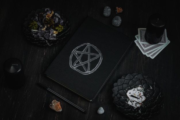 Livre en cuir noir avec un signe magique pierres rituelles bougies fleurs séchées et cartes de tarot sur un bla