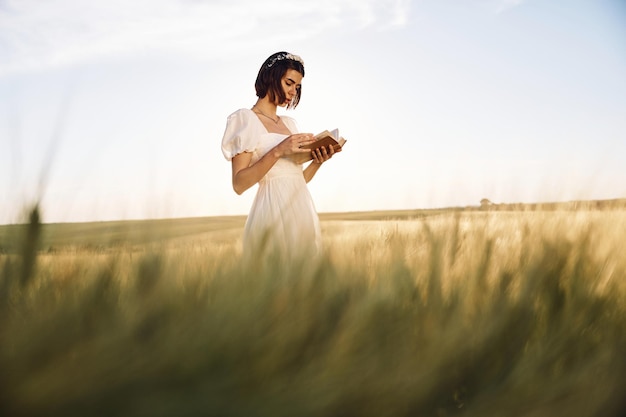 Avec un livre dans les mains Belle jeune mariée en robe blanche est sur le terrain agricole à la journée ensoleillée