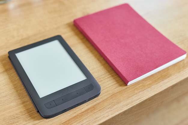 Photo livre électronique noir avec écran vide et bloc-notes rouge sur la vue d'angle de table en bois.