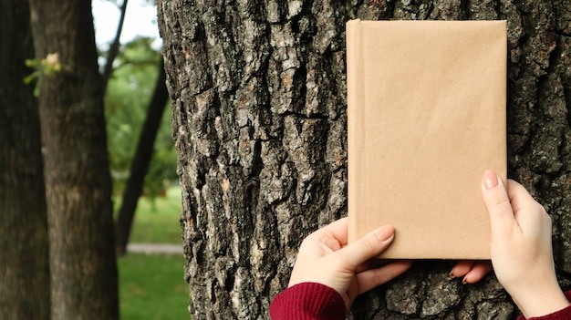 Un livre fermé dans une couverture en papier kraft dans des mains féminines sur fond d'écorce d'arbre dans le parc. Espace de copie. Le concept de lecture, de loisirs et de loisirs, d'étude et d'éducation.