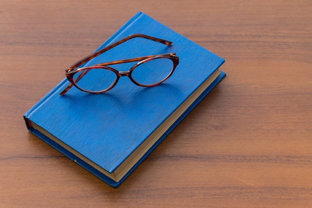 Livre fermé et lunettes sur fond de bois