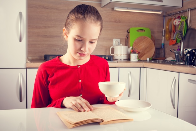 Livre de lecture d'adolescente avec une tasse de thé à la cuisine