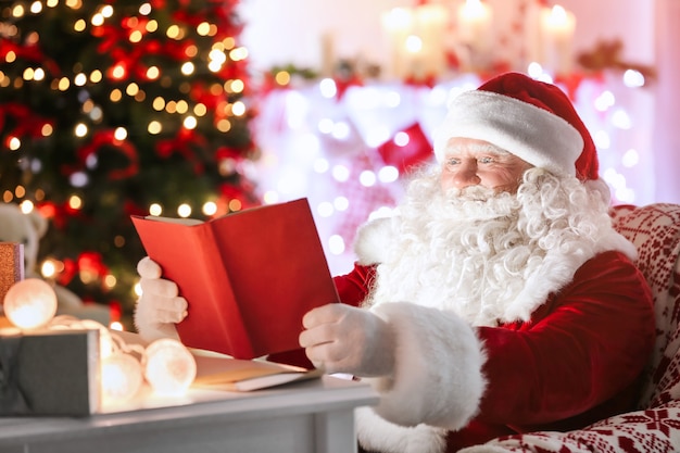 Livre de lecture authentique du Père Noël à table dans une chambre décorée pour Noël