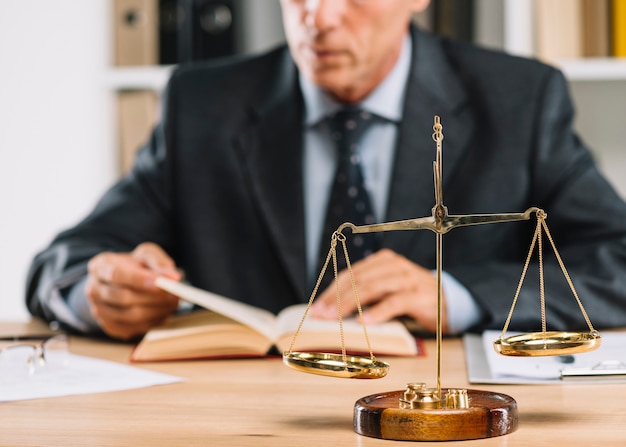Photo livre de lecture d'avocat mâle mature avec l'échelle de la justice sur le bureau