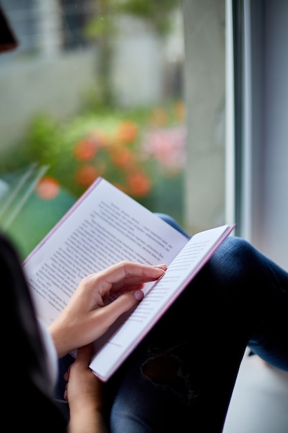 Livre de lecture de belle jeune femme près de la fenêtre à la maison.