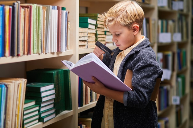 Livre de lecture de garçon d'âge préscolaire dans la bibliothèque avec patience, garçon enfant caucasien est concentré sur l'éducation