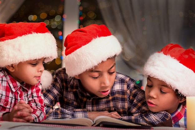 Livre de lecture de garçons à Noël. Enfants en chapeaux de Père Noël lisant. Lire des histoires de Noël la nuit. Ambiance de vacances calme.