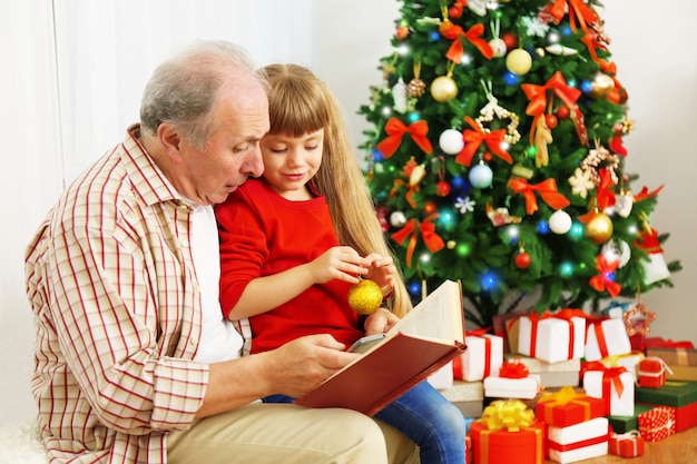 Livre de lecture d'un homme âgé avec sa petite-fille dans un salon décoré pour Noël