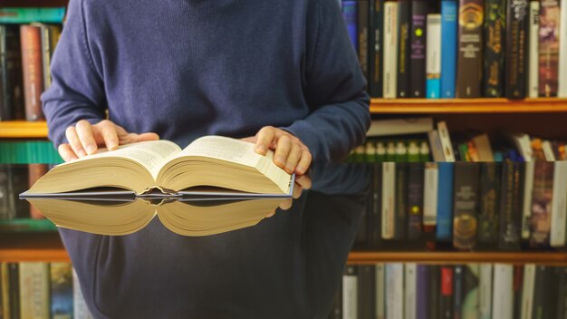 Livre de lecture homme blanc à une table en verre et librairie avec beaucoup de livres.