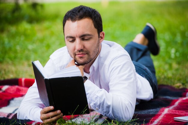 Livre de lecture jeune homme d'affaires couché dans le parc