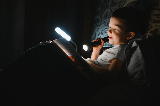 Livre de lecture et lampe de poche Jeune garçon en vêtements décontractés allongé près de la tente le soir