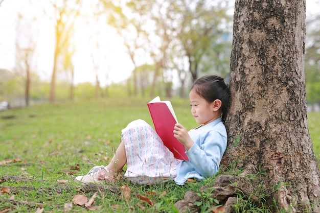 Livre de lecture de petite fille en été parc en plein air s&#39;appuyer contre le tronc d&#39;arbre dans le jardin d&#39;été.