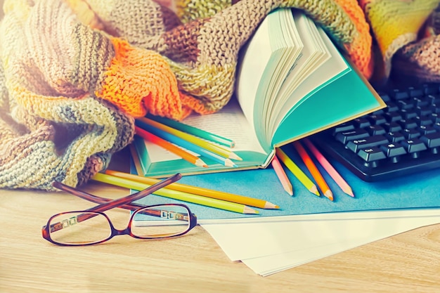 Un livre, des lunettes, une couverture tricotée et des crayons de couleur sur le fond en bois.