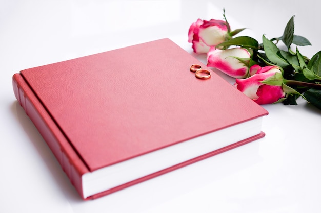 Livre de mariage ou album couvert de cuir rouge avec deux alliances et trois roses