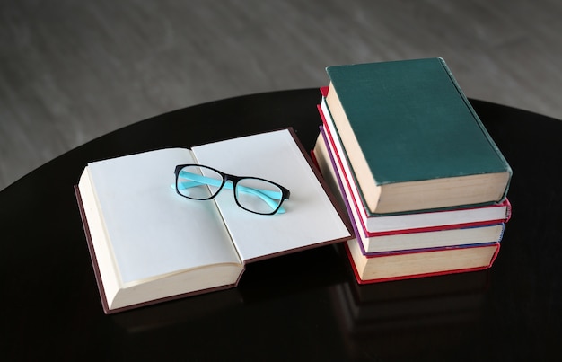 Livre ouvert, livres à couverture rigide et lunettes sur table en bois