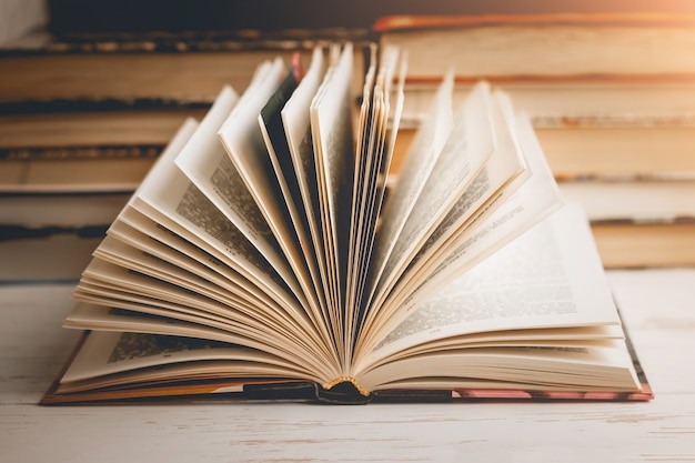 Un livre ouvert avec des lunettes sur une table en bois dans le contexte d'un ensemble de livres, tonification vintage.