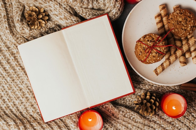 Livre ouvert avec des pages blanches, des biscuits sur une assiette et des bougies sur une couverture tricotée