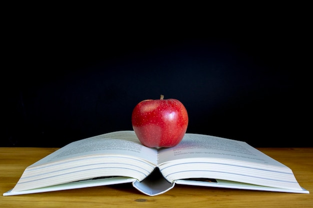 Livre ouvert et une pomme rouge devant le tableau noir