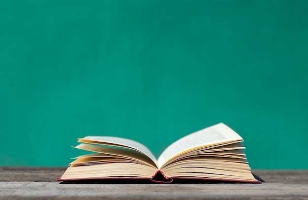 Un livre ouvert se trouve sur une table en bois grise sur fond turquoise