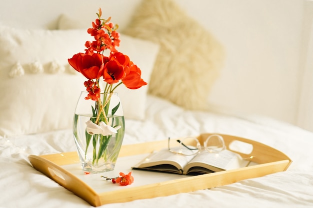 Livre ouvert et vase tulipes rouges sur un plateau sur le lit
