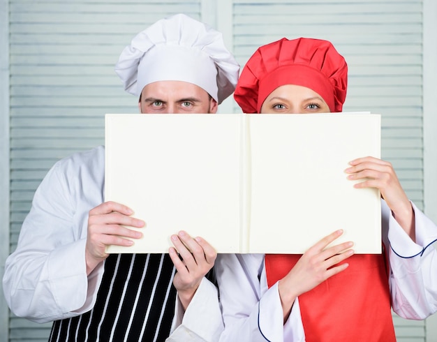 Livre des recettes de famille Guide de cuisine Selon la recette Manand femme chef cache les visages derrière un livre ouvert Un gars et une fille lisent des recettes de livre Concept culinaire La famille apprend la recette Améliorer les compétences culinaires