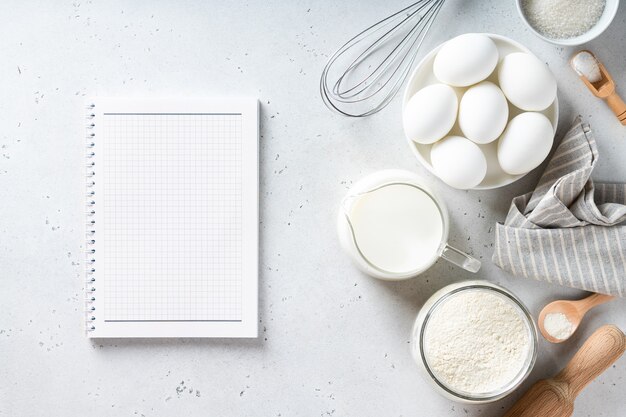 Livre de recettes et ingrédients de boulangerie sur une table blanche vue d'en haut