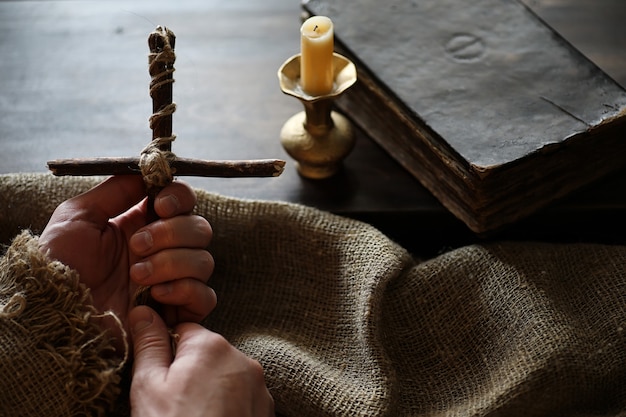 Livre religieux antique et croix en bois sur le fond d'un bois et d'une toile de jute