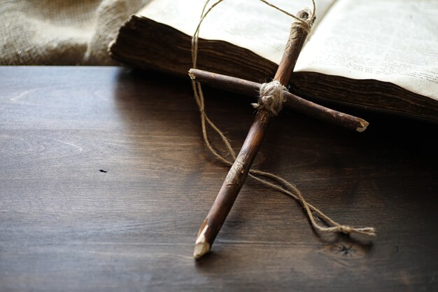 Livre religieux antique et croix en bois sur le fond d'un bois et d'une toile de jute