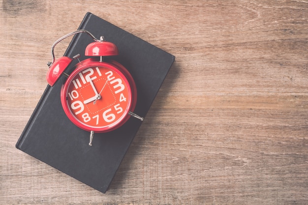 Livre de vue de dessus et horloge rouge sur fond de planche de bois. Temps pour lire le concept