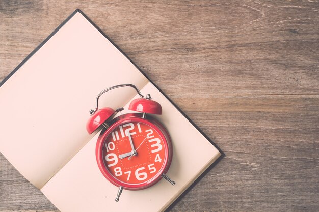 Livre de vue de dessus et horloge rouge sur fond de planche de bois. Temps pour lire le concept