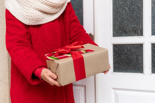 Livrer habillé en manteau rouge tenant des coffrets cadeaux près de la porte blanche à la veille des fêtes de Noël et du nouvel an.