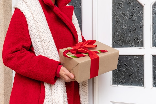 Livrer habillé en manteau rouge tenant des coffrets cadeaux près de la porte blanche à la veille des fêtes de Noël