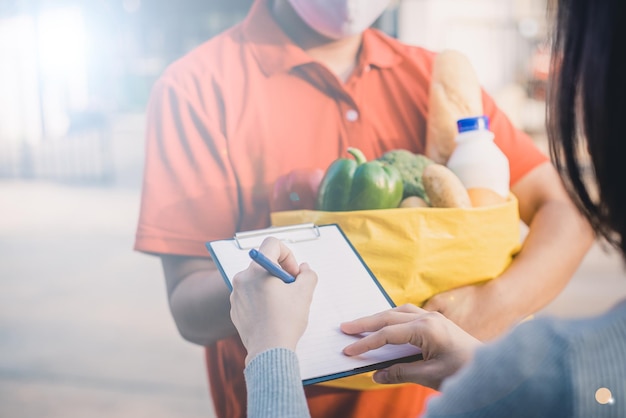 Livrer un homme portant un masque facial en uniforme rouge manipulant un sac jaune de légumes de lait de fruits alimentaires