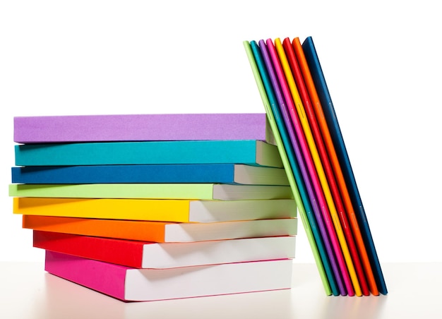 Les livres et les cahiers de couleur arc-en-ciel sont décrits empilés sur une table blanche