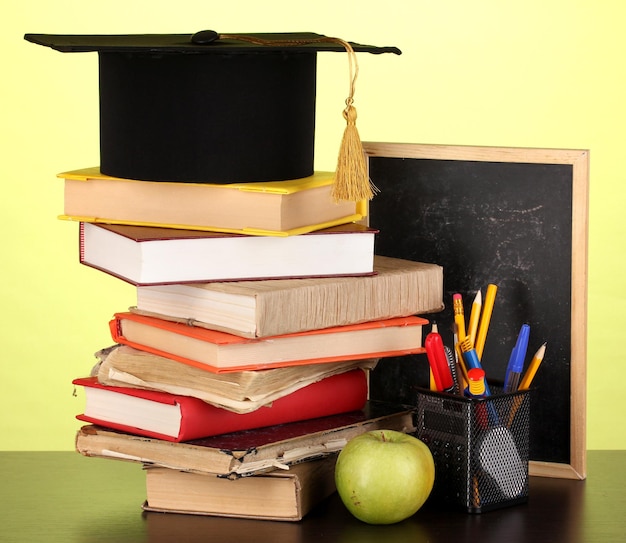 Livres et casquette magister contre commission scolaire sur table en bois sur fond vert