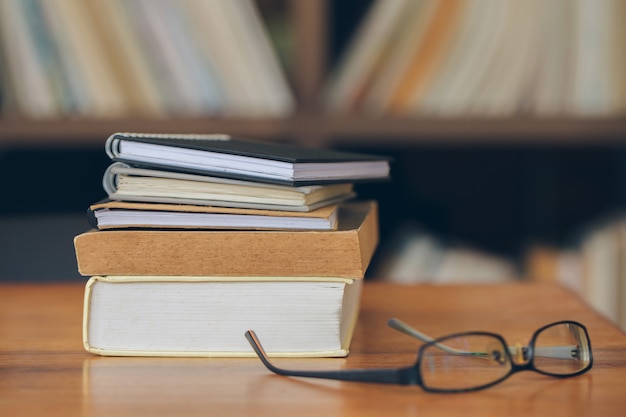 livres empilés et lunettes sur la vieille table en bois de la bibliothèque.