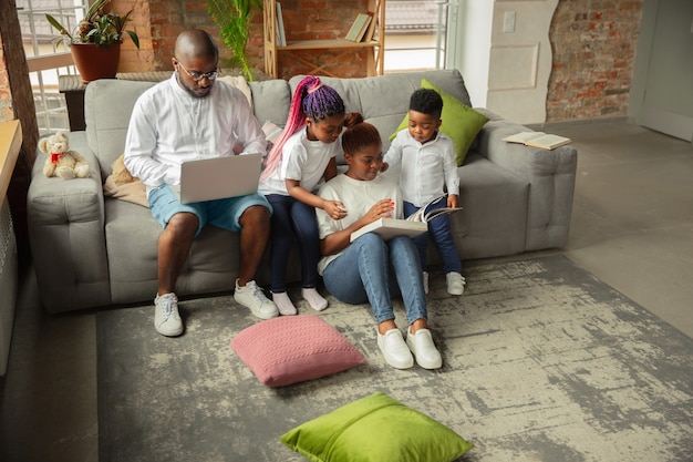 Livres lisant une famille africaine jeune et gaie pendant l'isolement de la quarantaine