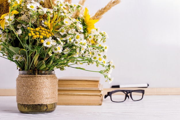 Livres, lunettes, marqueurs et un bouquet de fleurs dans un vase sur blanc