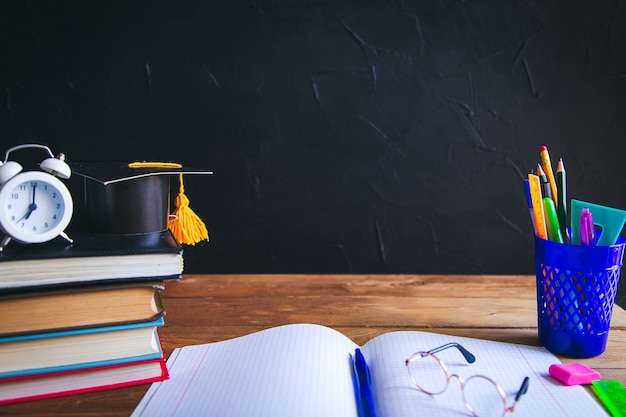 Livres, matériel d'écriture, lunettes, cahier et réveil sur le bureau. Fond noir. Concept d'apprentissage et d'auto-éducation. Mise au point sélective.