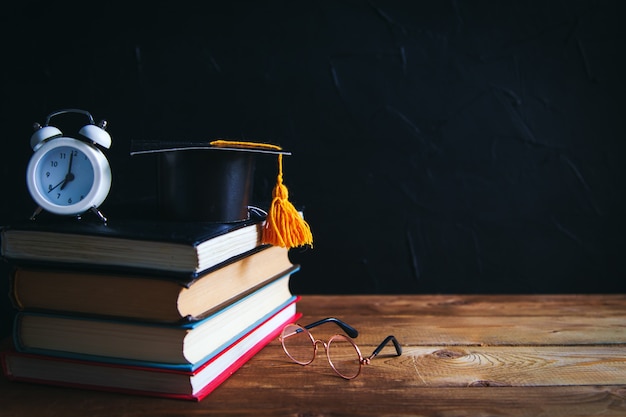 Livres, matériel d'écriture, lunettes, cahier et réveil sur le bureau. Fond noir. Concept d'apprentissage et d'auto-éducation. Mise au point sélective.