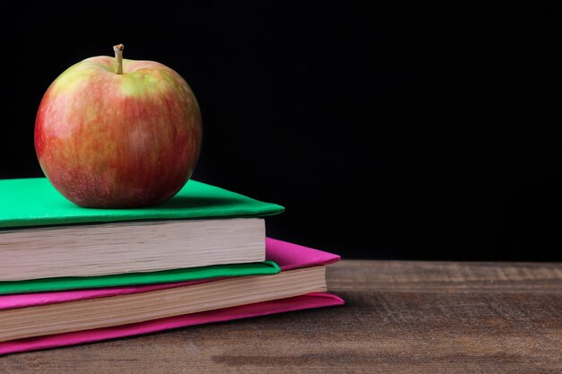 Des livres et une pomme sur une table en bois marron sur fond noir. notion d'éducation